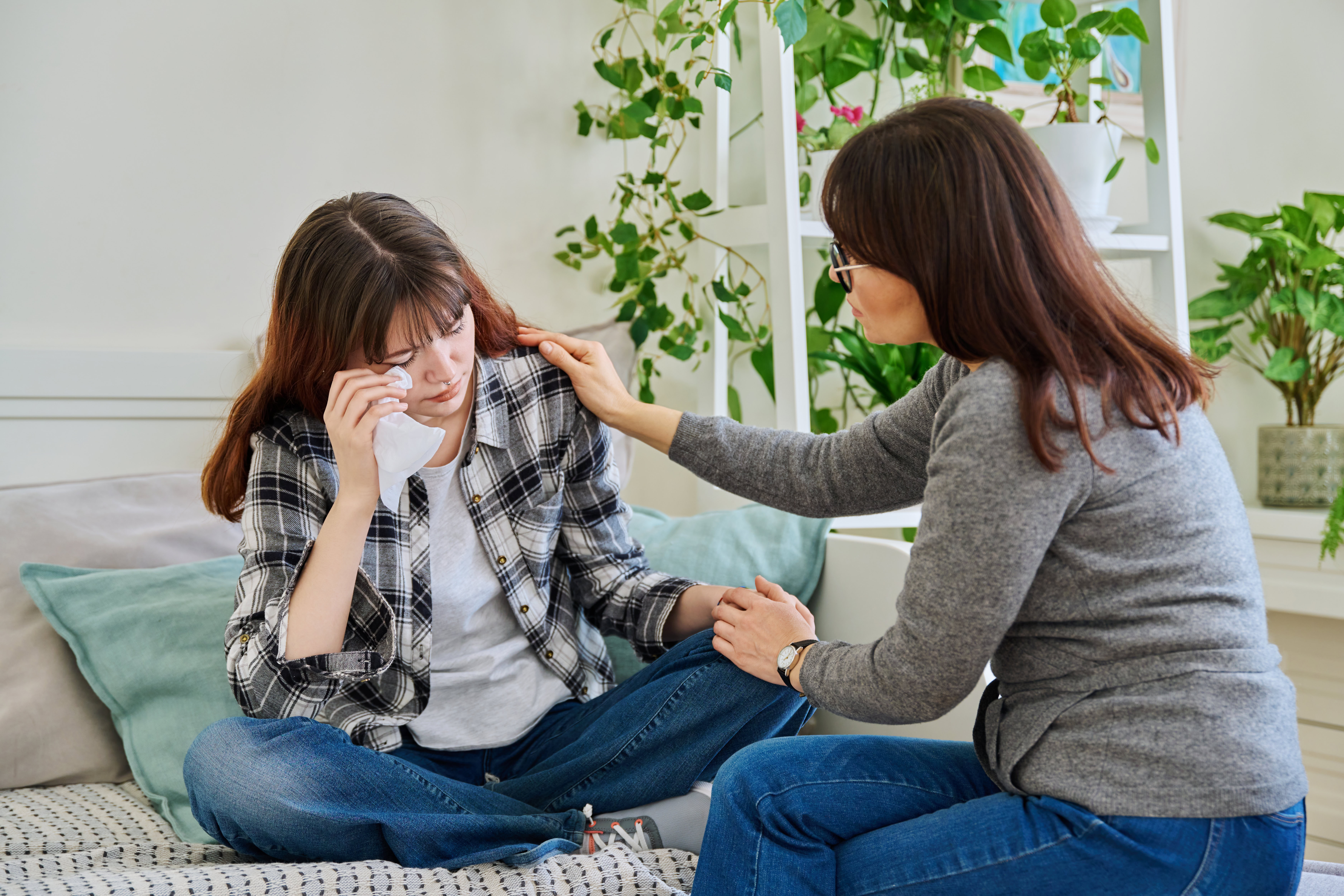 Upset sad crying daughter teenager sitting together with mother on couch at home Upset sad crying daughter teenager sitting together with mother on couch at home. Family, communication, motherhood, friendship, relationship between parent and teen daughter concept